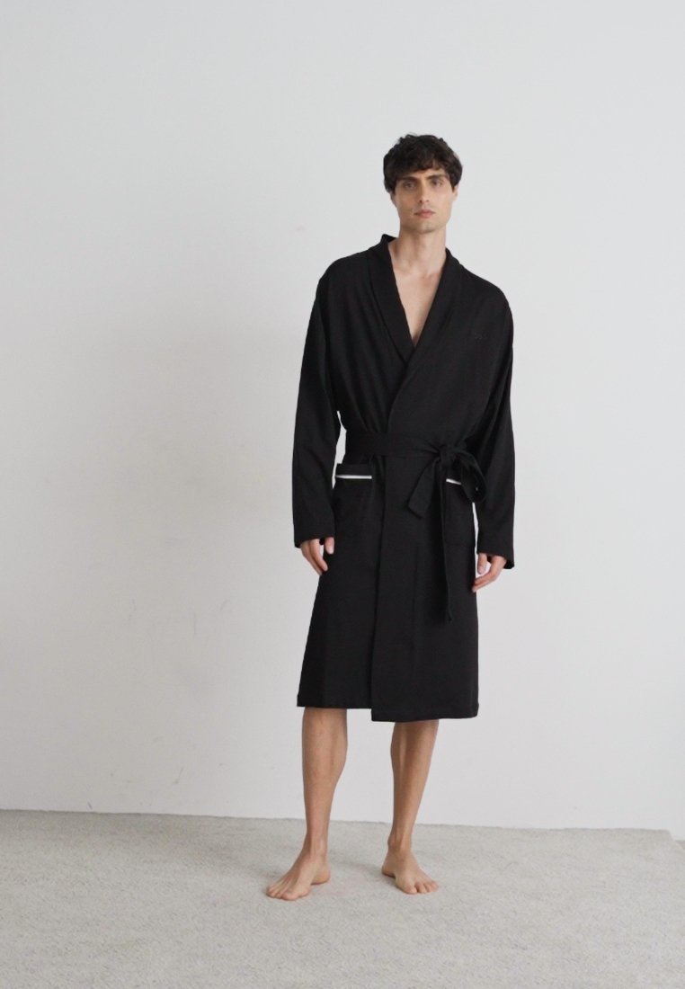 Peignoir noir, longueur genoux, en tissu doux, avec un col châle, des manches longues, une ceinture à nouer et deux poches avant.