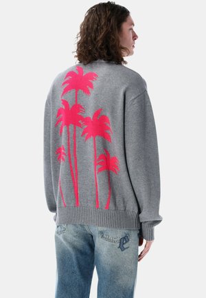 Maglione grigio con un vivace design di palma rosa sulla schiena, con polsini e orlo a coste. Abbinato a jeans blu chiaro.