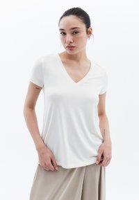 Camiseta blanca de cuello en V con mangas cortas, textura suave y un corte relajado, combinada con pantalones anchos beige.