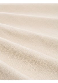 Világos bézs szövet, textúrált szövéssel, amelyek lágy redők és finom tónusváltozások jellemzik, különböző textilipari alkalmazásokhoz megfelelő.