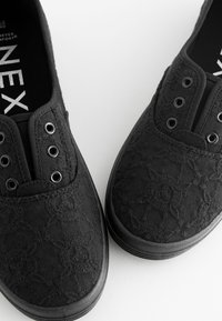 Sorte lærredsko med et tekstureret blomsterprint, udstyret med metaløjer og en gummisål, designet til komfort og afslappet brug.