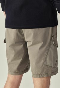 Beige cargo nadrág zsebekkel, könnyű szövetből készült. Lazább szabású és megerősített szegéllyel rendelkezik a tartósság érdekében.