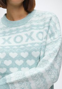 Gai zili džemperis ar apaļo kaklu, kas rotāts ar sirds un "XOXO" motīvu baltā krāsā. Izgatavots no mīksta, teksturēta adījuma materiāla.