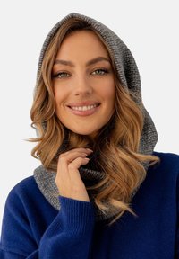 Szary dziany szalik z kapturem o teksturowanym wykończeniu, noszony na niebieskim swetrze. Projekt charakteryzuje się dopasowaniem wokół szyi i głowy.