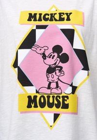 Witte T-shirt met een grafisch ontwerp van Mickey Mouse in zwart en roze, omlijnd door een gele diamant en zwart/wit geblokte accenten.
