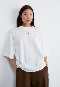 Hvit oversized t-skjorte laget av bomull med rund hals og korte ermer; har en liten svart Puma-logo på brystet.