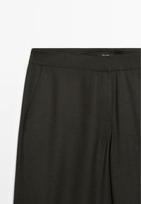 Donkergrijze stof van een broek met een tailleband en zijzakken, die een slank en minimalistisch ontwerp benadrukt.