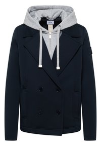 Manteau bleu marine à double boutonnage porté sur un sweat à capuche zippé gris clair avec cordons et capuche.