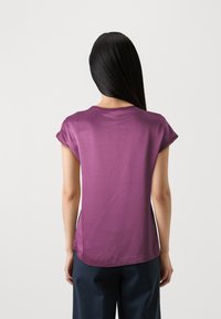 T-shirt viola a maniche corte con scollatura rotonda e texture liscia, dotata di cuciture laterali e vestibilità rilassata.