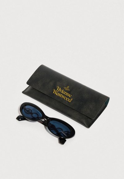 Gafas de sol ovaladas negras con lentes azules y acentos únicos en forma de cadena, acompañadas de un estuche negro texturizado con branding en dorado.