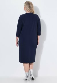 Marineblaue, knielange Kleid mit Dreiviertelärmeln und einem subtilen Schlitz an den Manschetten. Kombiniert mit silbernen Knöchelstiefeln. Glatte Stofftextur.
