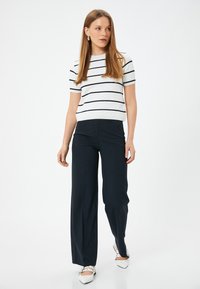Blusa de manga corta a rayas en blanco y azul marino, combinada con pantalones anchos de tiro alto en azul marino y zapatos blancos de punta.