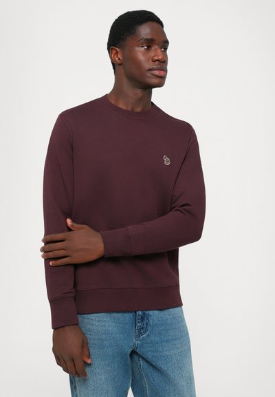 Burgundy sweatshirt in soft material, round neckline, and ribbed cuffs and hem. Features a small embroidered logo on the chest.