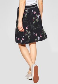 Musta hame, jossa on kukkakirjailua, liehuva muotoilu, joustava vyötärö ja polven mittainen leikkaus. Yhdistetty vaaleavärisiin kenkiin.