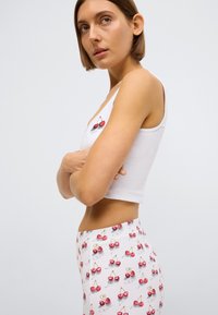 Débardeur blanc court avec un motif de cerise, associé à des leggings de couleur claire ornés d'un motif répétitif de cerises et de texte en écriture cursive.