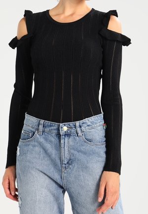 Zwarte gebreide top met een cold shoulder ontwerp, geribbelde textuur en ruches; gecombineerd met lichtblauwe distressed denim jeans.