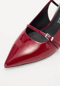Chaussure à talon haut en cuir verni rouge avec un bout pointu et une fine sangle dotée d'une boucle en argent. Doublure et semelle noires.