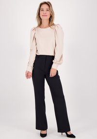 Beige blouse met lange mouwen en pofschouders, gecombineerd met zwarte op maat gemaakte broek met een rechte snit en een gladde textuur. Zwarte hakken inbegrepen.