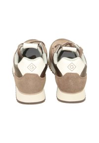 Paire de baskets marron et blanches vues de dos, montrant des détails en daim et en cuir avec un logo "G" sur la languette du talon.