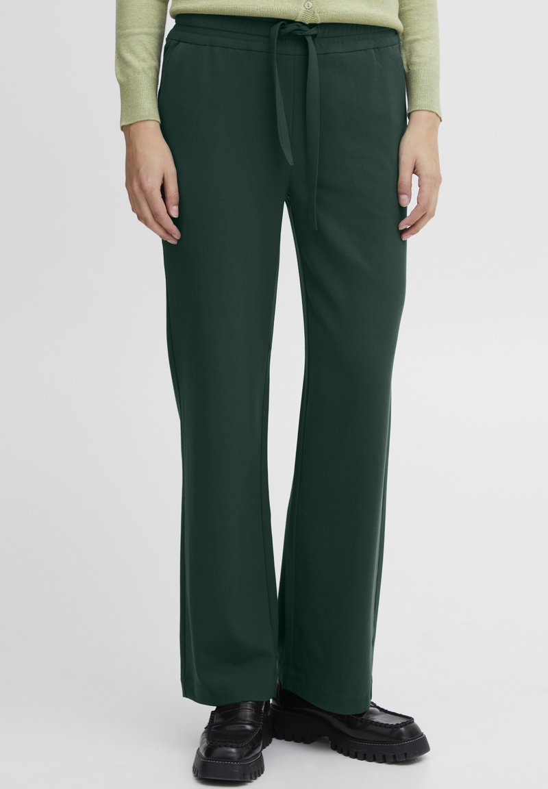 Green wide-leg pants made of smooth fabric, featuring a tied waistband and plain design. Pairing black chunky shoes at the bottom.