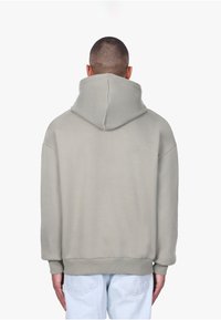 Sweat-shirt à capuche gris clair avec une coupe décontractée, texture douce, poignets et ourlet côtelés, doté d'une grande capuche et sans logos visibles.
