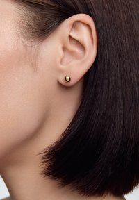 Złota kolczyk wkręcany o gładkim, zaokrąglonym wzorze. Produkt noszony jest na małżowinie usznej, doskonale uzupełniając krótki, prosty, ciemny włos.