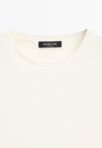Světle krémový svetr s kulatým výstřihem a ribbovaným límcem, uvnitř výstřihu černý štítek s nápisem "Massimo Dutti Made in China".