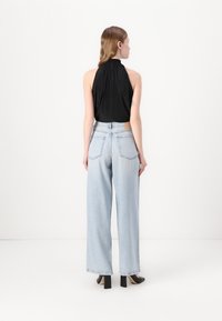 Zwarte geplooide haltertop gecombineerd met lichtblauwe wijde jeans. De outfit heeft een strakke lijn en subtiele stiksels. Zwarte hakken.
