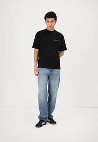 Black short-sleeve t-shirt with a crew neck, paired with light blue loose-fit jeans and black sneakers featuring white stripes.