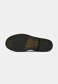 Suela de zapato de goma negra con un patrón de relieve texturizado que presenta surcos y un logo elevado. La forma general es plana y resistente.