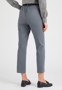 Grijze op maat gemaakte broek met een vlakke voorzijde, elastische tailleband en twee achterzakken, gecombineerd met zwart leren schoenen. Glad stoftextuur.