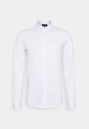 Camisa branca de manga longa feita de algodão, com colarinho clássico, frente com botões e uma textura lisa sem padrões visíveis.