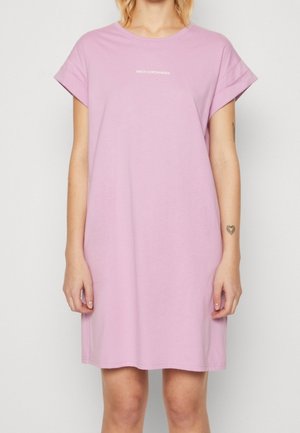 Kvinde iført en løs, kortærmet lavendelkjole med "MSCH COPENHAGEN" trykt i hvidt på brystet.