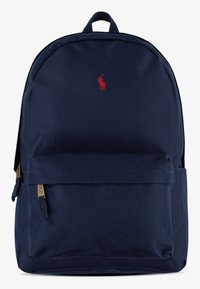 Námořnický plátěný batoh s přední kapsou na zip, červeným logem, vycpanými zády a horním madlem. Má nastavitelné ramenní popruhy.