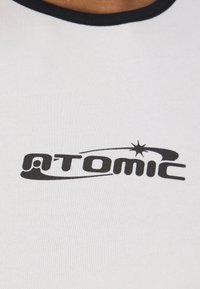 Balta medvilninė marškinėliai su juodu apykaklės iškirpimu. Yra didelis juodas "ATOMIC" logotipas su žvaigždės grafika ir kreivomis detalėmis.
