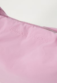 Ružová textilná taška s ťahaným logom "SAMSOE SAMSOE", hladkou textúrou a strieborným zipsovým detailom. Jednoduchý, čistý dizajn.