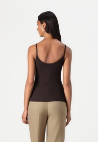 Top en coton marron ajusté avec des fines bretelles, texture lisse et décolleté rond. Associé à un pantalon beige, vu de dos.