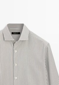 Chemise à boutons rayée présentant des fines rayures verticales en blanc et couleurs foncées, avec un col classique et une texture de tissu lisse.