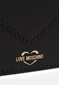 Czarny skórzany portfel z złotym logo "LOVE MOSCHINO" i wzorem serca. Posiada kontrastowe przeszycia wzdłuż krawędzi. Gładka tekstura.