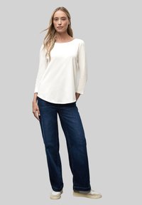Weißes Longsleeve mit rundem Ausschnitt, kombiniert mit dunkelblauen weit geschnittenen Jeans. Das Outfit wird von neutralen Sneakers abgerundet.