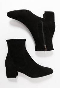 Un paio di stivaletti neri in suede con cerniera laterale e tacco basso su sfondo bianco.