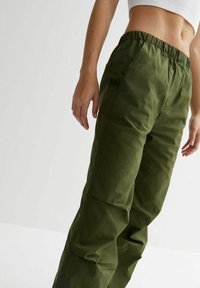 Zelené cargo kalhoty s elastickým pasem a kapsami po stranách. Vyrobené z látky s jemně texturovaným povrchem, mají volný střih a zúžené nohavice.