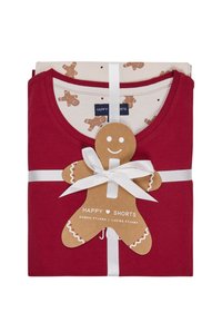 Rode katoenen pyjama's opgevouwen met een crèmekleurig shirt met peperkoekpatronen. Vastgemaakt met een wit lint en een label in de vorm van een peperkoek.