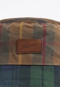 Tessuto a quadri caratterizzato da strisce marroni, verdi, rosse e gialle. Un'etichetta in pelle marrone con la scritta "Millerain Fabric" è ben in vista.