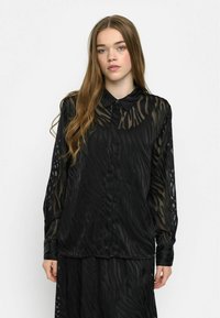 Sort gennemsigtig bluse med zebrastribemønster, knaplukning foran og lange ærmer. Blødt materiale med en afslappet pasform.