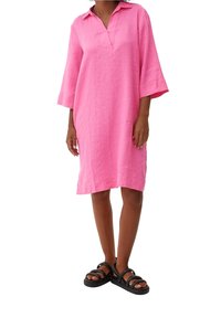 Rosa Leinenkleid mit Kragen, Dreiviertelärmeln und lockerer Passform. Das Modell trägt schwarze Riemchensandalen für den Kontrast.
