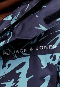 Giacca navale con un motivo astratto turchese, chiusura con zip e logo "JACK & JONES" bianco nella zona del petto. Tessuto testurizzato.