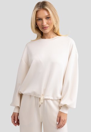 Crème-kleurige sweatshirt met een relaxte pasvorm, ronde halslijn en ballonsleeves. Heeft een trekkoord aan de onderzijde voor een verstelbare pasvorm.