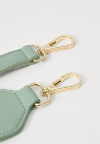 Šviesiai žalias odinis dirželis su šešiakampio forma ir aukso metalinėmis sagtimis. Aparatūra apima išgraviruotą "VALENTINO" detalę.