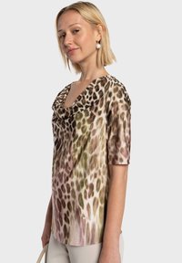 Haut à col bénitier en tissu doux et léger présentant un imprimé animal texturé dans des tons de vert et de rose avec des manches courtes.